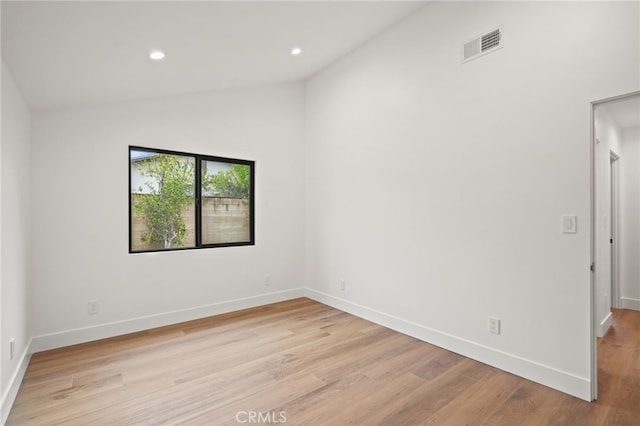 empty room featuring visible vents, light wood-style flooring, baseboards, and vaulted ceiling