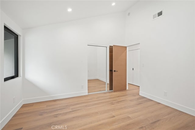 spare room featuring visible vents, baseboards, light wood-type flooring, recessed lighting, and a high ceiling