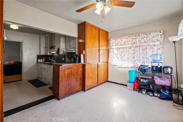 kitchen featuring baseboards, light floors, brown cabinets, a ceiling fan, and a sink