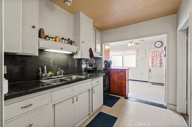 kitchen with dark countertops, stainless steel range with gas stovetop, backsplash, and a sink