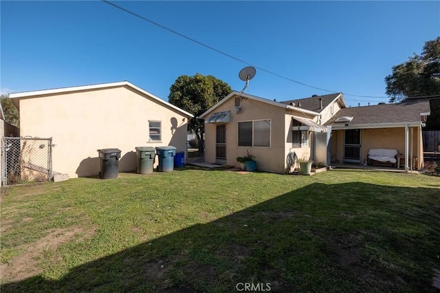 rear view of house with a lawn, fence, and stucco siding