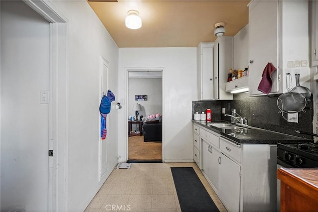 kitchen with dark countertops, backsplash, white cabinetry, and a sink