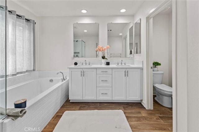 full bathroom with toilet, a bath, wood finished floors, and a sink