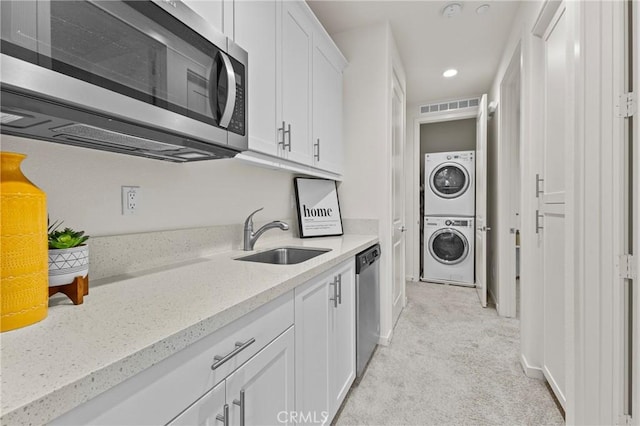 kitchen featuring visible vents, a sink, appliances with stainless steel finishes, white cabinets, and stacked washer / drying machine