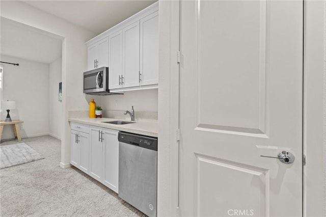 kitchen with a sink, light countertops, white cabinets, appliances with stainless steel finishes, and light carpet