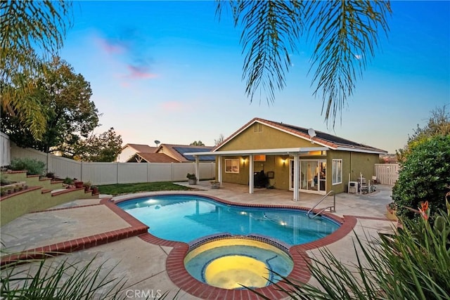 pool at dusk featuring a patio, a fenced backyard, and a pool with connected hot tub