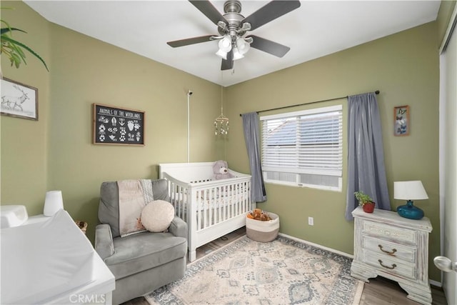 bedroom with ceiling fan, baseboards, a crib, and wood finished floors