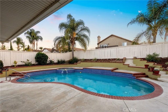 pool at dusk featuring a pool with connected hot tub, a fenced backyard, and a patio area