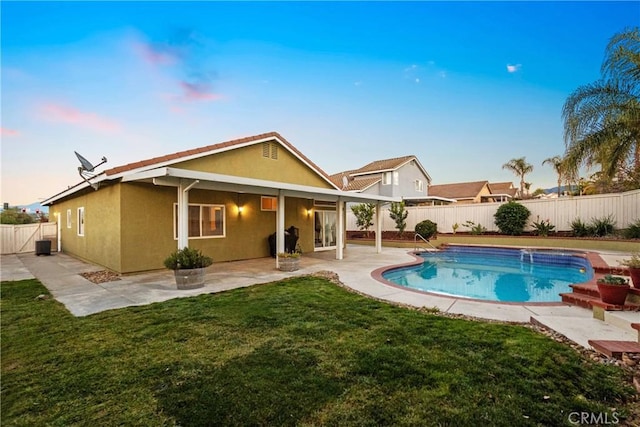 back of house at dusk featuring stucco siding, a lawn, a patio, a fenced backyard, and a fenced in pool