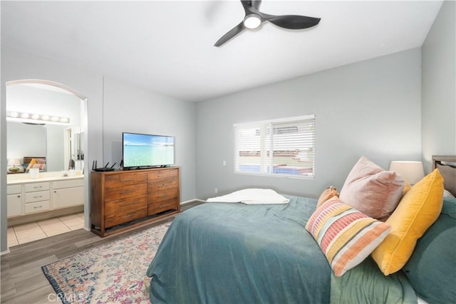 bedroom featuring arched walkways, ensuite bathroom, light wood-type flooring, and ceiling fan