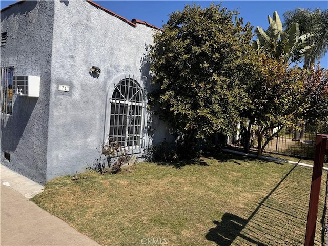 view of side of home featuring stucco siding, a lawn, and fence