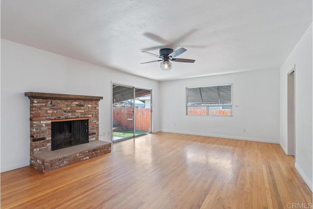 unfurnished living room with a brick fireplace, wood finished floors, and baseboards