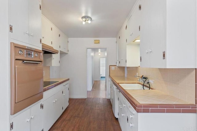 kitchen featuring oven, under cabinet range hood, backsplash, dark wood-style floors, and white cabinets