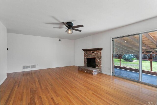 unfurnished living room with visible vents, a brick fireplace, a ceiling fan, and wood finished floors