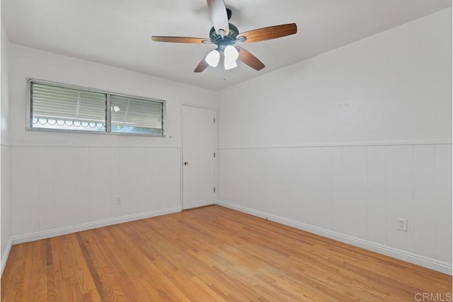 unfurnished room featuring wainscoting, ceiling fan, and light wood-style floors