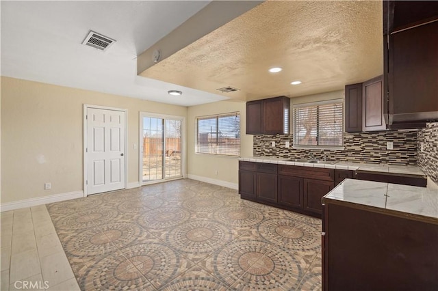 kitchen featuring visible vents, backsplash, baseboards, and a sink