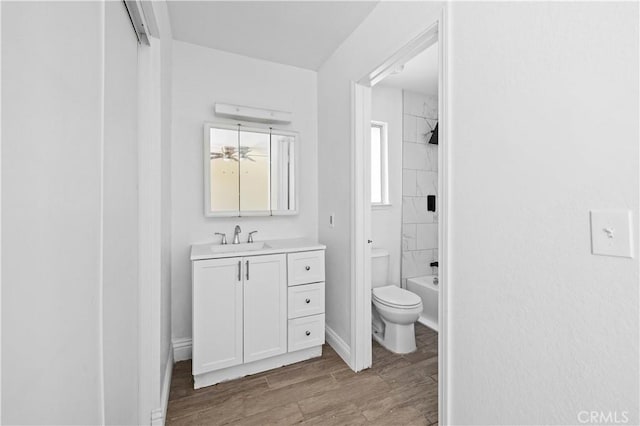 bathroom with toilet,  shower combination, wood finished floors, vanity, and a ceiling fan