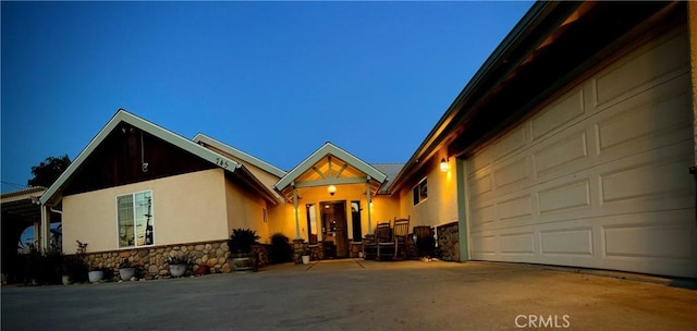 view of front of house featuring stone siding, a garage, driveway, and stucco siding