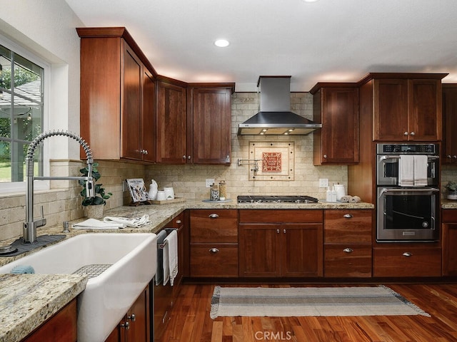 kitchen featuring dark wood-style flooring, backsplash, a sink, appliances with stainless steel finishes, and wall chimney exhaust hood