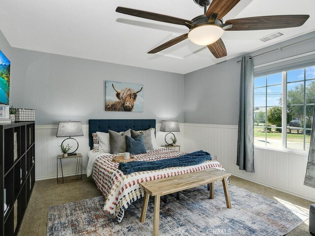 carpeted bedroom featuring visible vents, multiple windows, ceiling fan, and wainscoting
