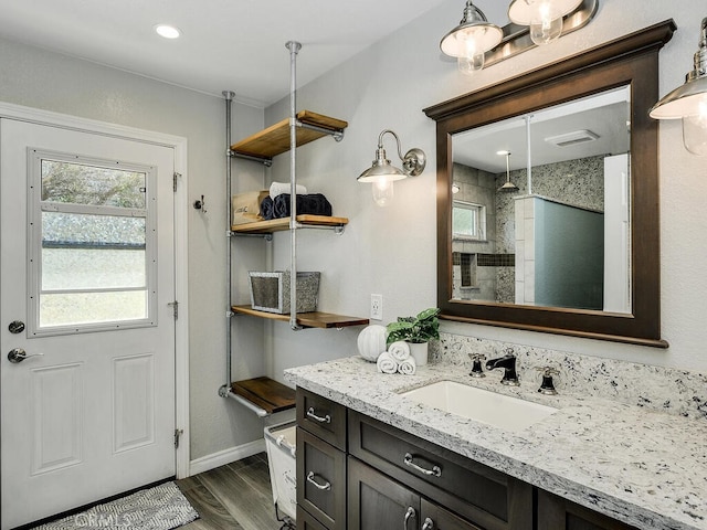 full bath featuring baseboards, wood finished floors, tiled shower, and vanity