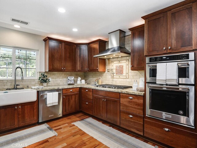 kitchen featuring visible vents, stainless steel appliances, wall chimney exhaust hood, a sink, and backsplash