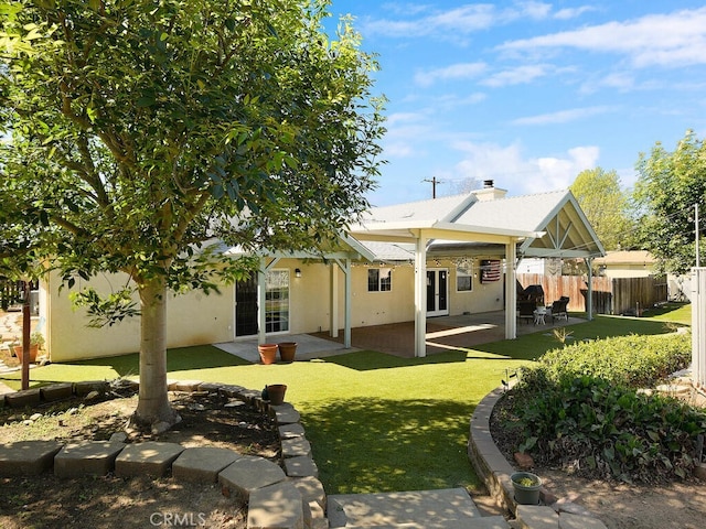 rear view of house featuring fence, a patio, stucco siding, a lawn, and french doors