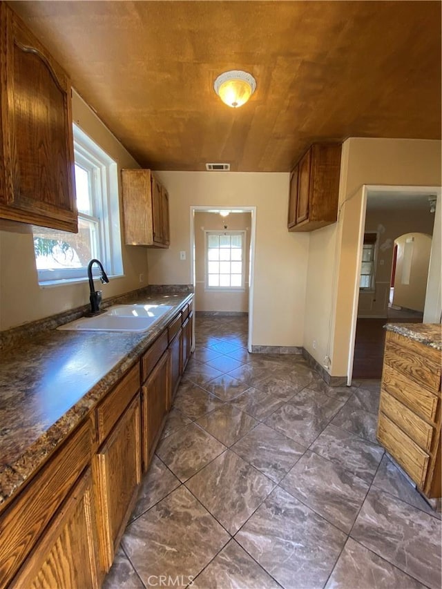 kitchen with baseboards, visible vents, a sink, dark countertops, and brown cabinets