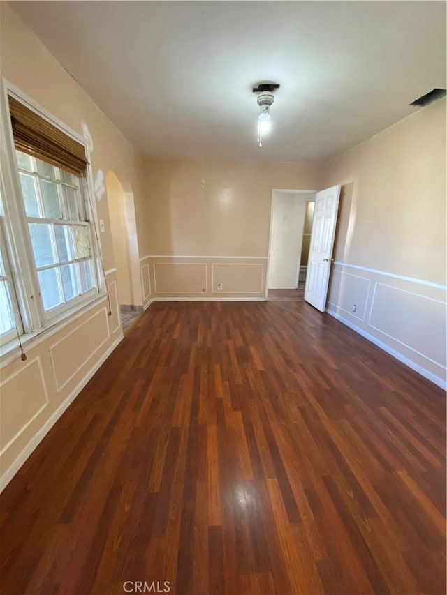 empty room featuring arched walkways, wood finished floors, and a decorative wall