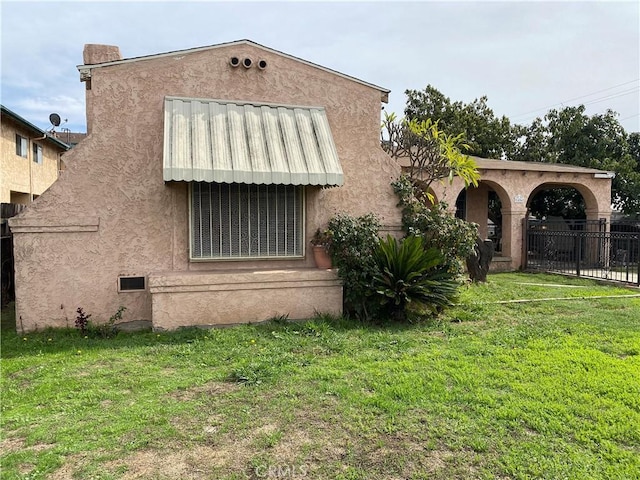 view of property exterior featuring stucco siding, a yard, and fence