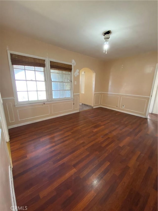 spare room featuring arched walkways, dark wood-style floors, wainscoting, and a decorative wall