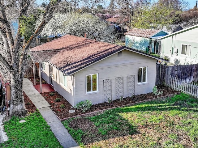 view of side of home with a lawn, roof with shingles, and fence