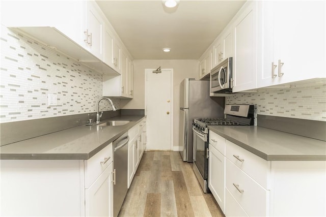 kitchen featuring light wood-type flooring, a sink, white cabinets, appliances with stainless steel finishes, and tasteful backsplash