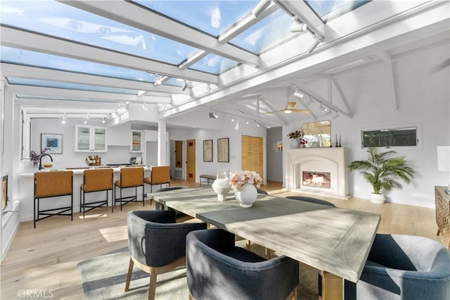 sunroom / solarium featuring a ceiling fan, a warm lit fireplace, a skylight, and rail lighting