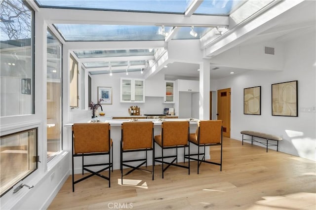 kitchen with light wood finished floors, visible vents, glass insert cabinets, a kitchen breakfast bar, and white cabinetry