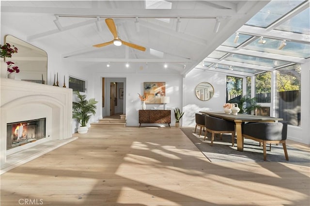 interior space with a glass covered fireplace, track lighting, vaulted ceiling with beams, and ceiling fan