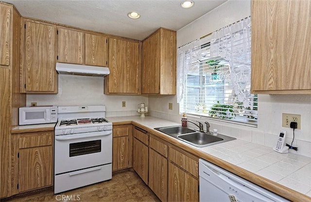 kitchen with white appliances, recessed lighting, under cabinet range hood, and a sink