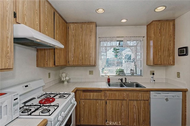 kitchen featuring white appliances, brown cabinetry, under cabinet range hood, and a sink