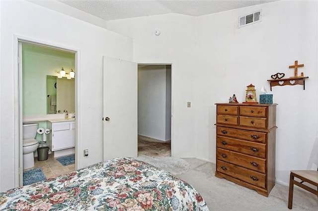 bedroom with a textured ceiling, visible vents, a sink, ensuite bathroom, and light carpet