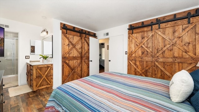 bedroom with a barn door, visible vents, and dark wood-style floors