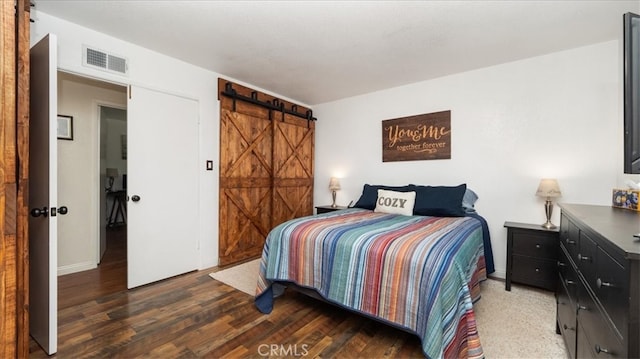 bedroom with a barn door, visible vents, and wood finished floors