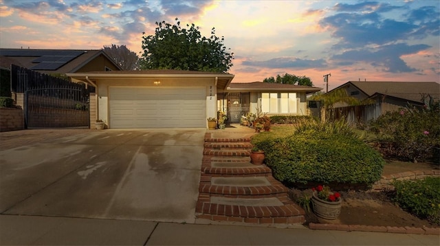 ranch-style house featuring fence, concrete driveway, stucco siding, an attached garage, and a gate