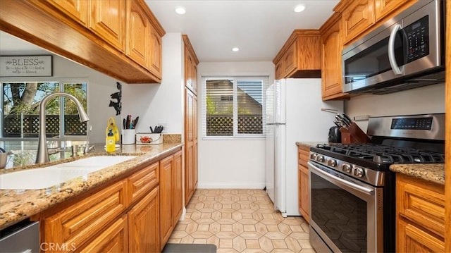 kitchen featuring light stone countertops, recessed lighting, brown cabinetry, stainless steel appliances, and a sink