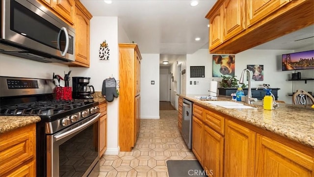 kitchen with light stone counters, light tile patterned floors, brown cabinets, appliances with stainless steel finishes, and a sink