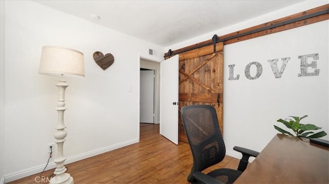 office with visible vents, baseboards, a barn door, and wood finished floors