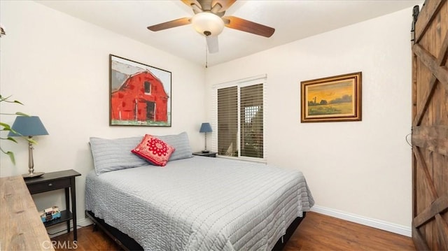 bedroom with a barn door, baseboards, wood finished floors, and a ceiling fan