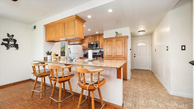 kitchen with visible vents, a sink, appliances with stainless steel finishes, a breakfast bar area, and a peninsula