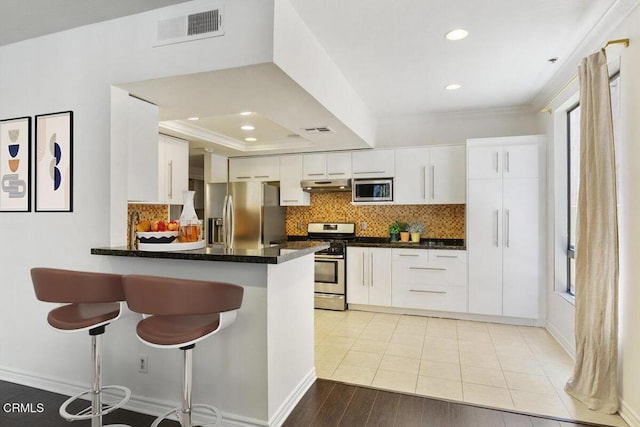 kitchen with dark countertops, visible vents, stainless steel appliances, under cabinet range hood, and crown molding