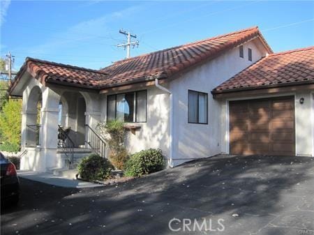 view of front facade featuring aphalt driveway, stucco siding, an attached garage, and a tile roof