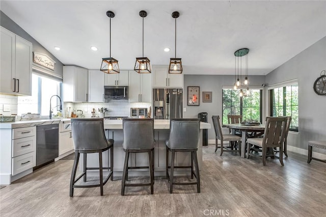 kitchen featuring vaulted ceiling, light wood-type flooring, backsplash, and stainless steel appliances